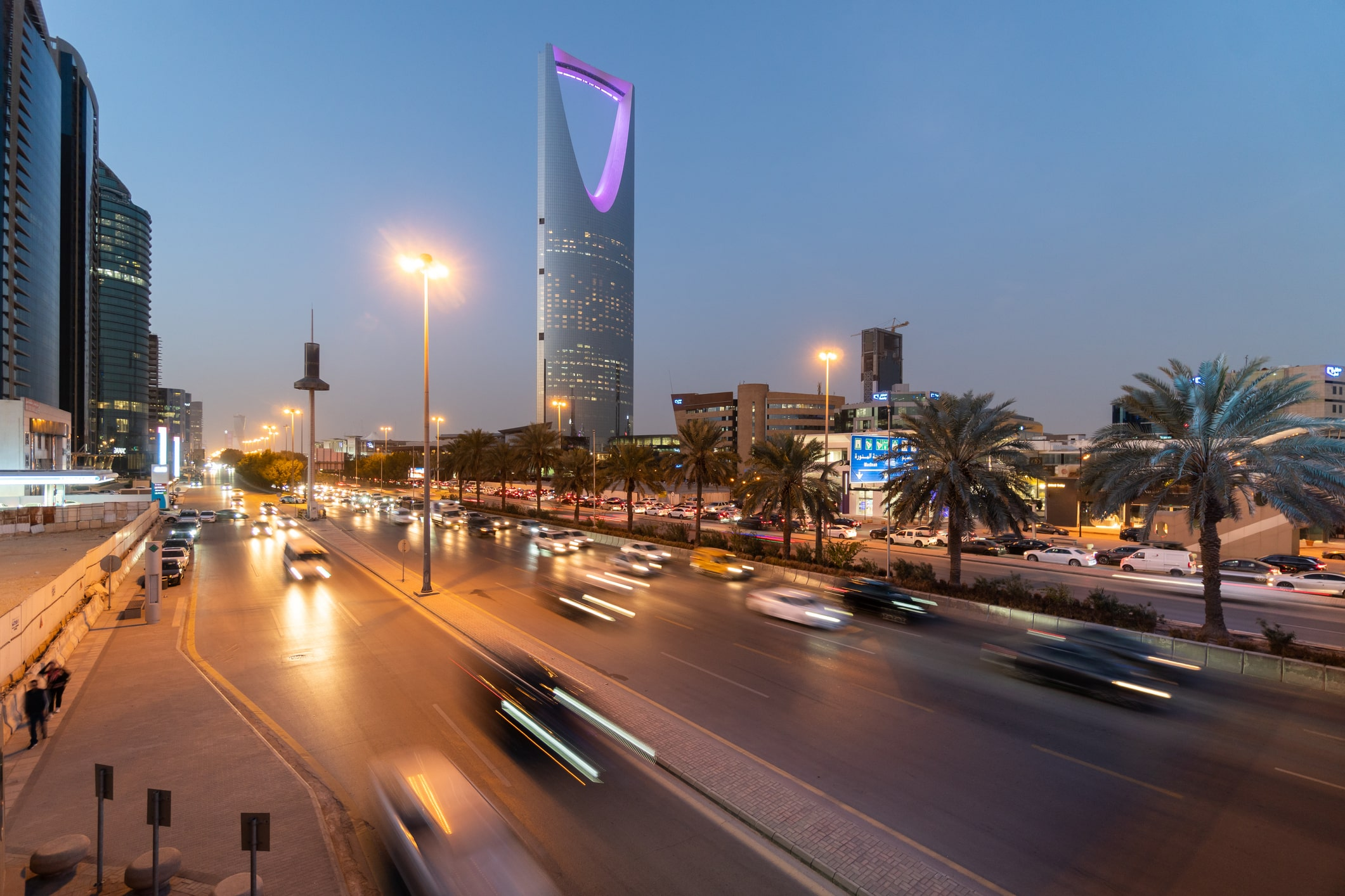 Riyadh business district at dusk with palms, traffic, and illuminated commercial towers