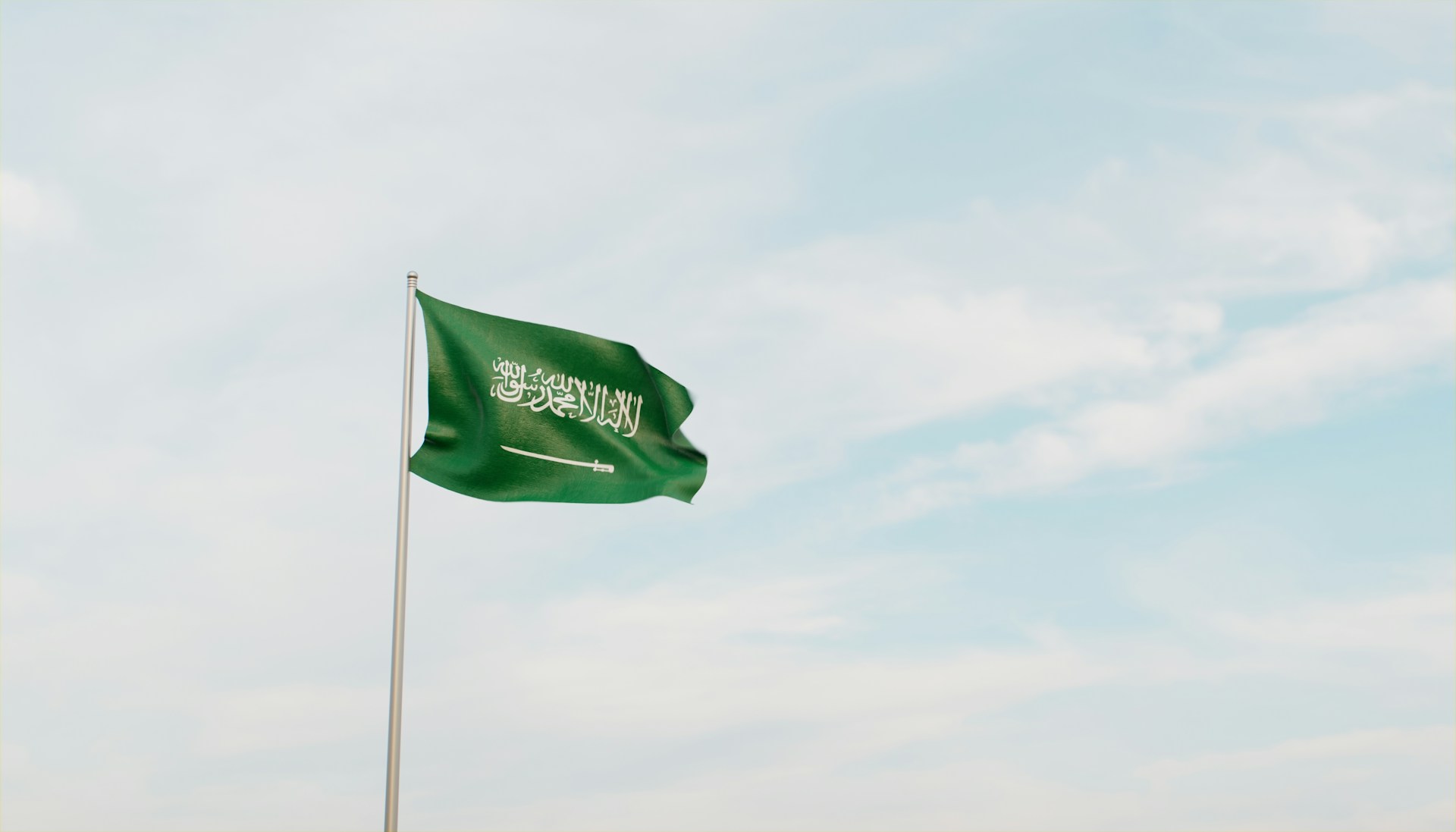 Saudi flag flying against a pale blue sky